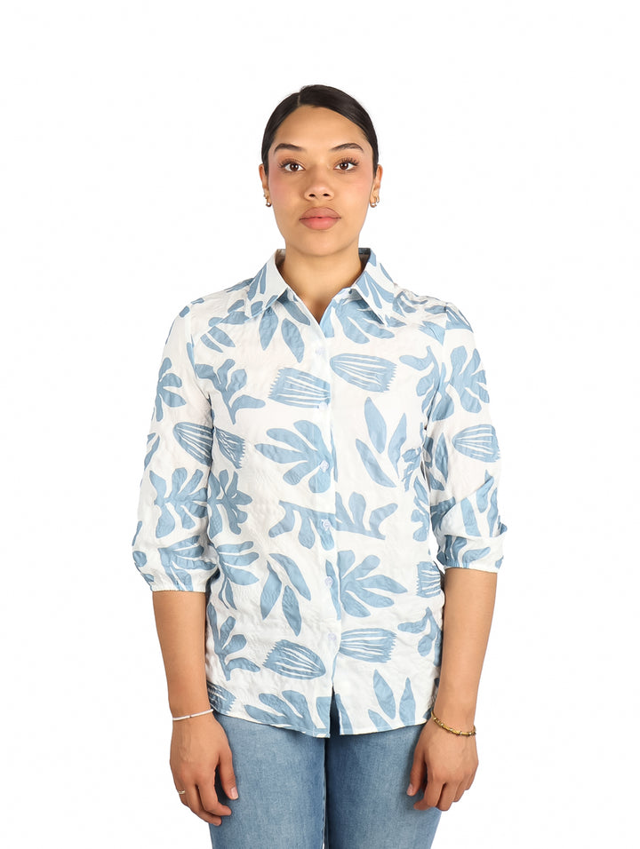 Mujer vistiendo una camisa blanca con estampado de hojas en color azul claro.