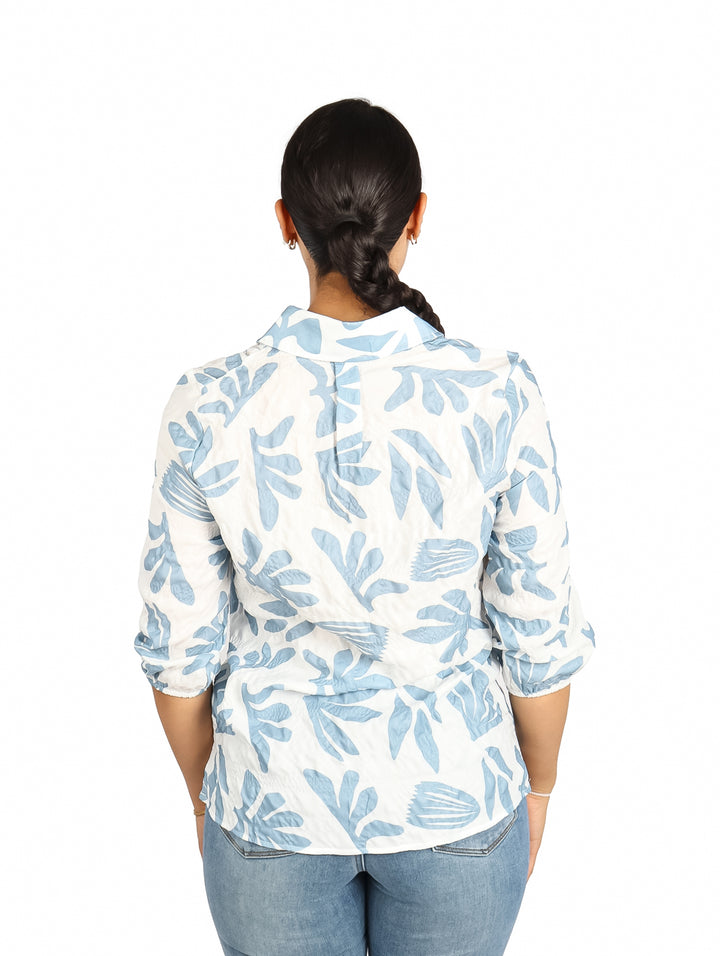 Mujer vistiendo una camisa blanca con estampado de hojas en color azul claro.