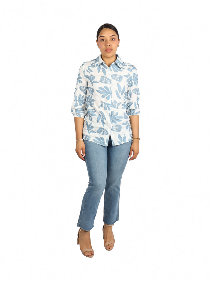 Mujer vistiendo una camisa blanca con estampado de hojas en color azul claro.