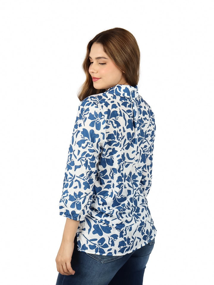 Mujer vistiendo una camisa blanca con estampado floral azul y pantalones jeans.