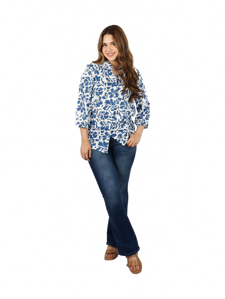Mujer vistiendo una camisa blanca con estampado floral azul y pantalones jeans.