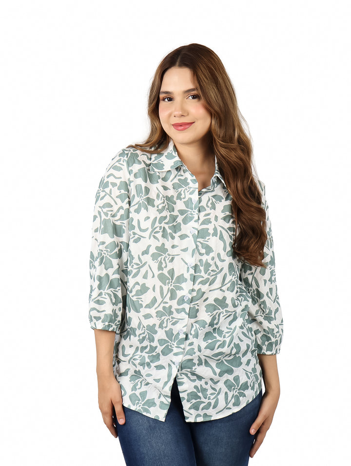 Mujer vistiendo una camisa blanca con estampado floral verde y pantalones azules.