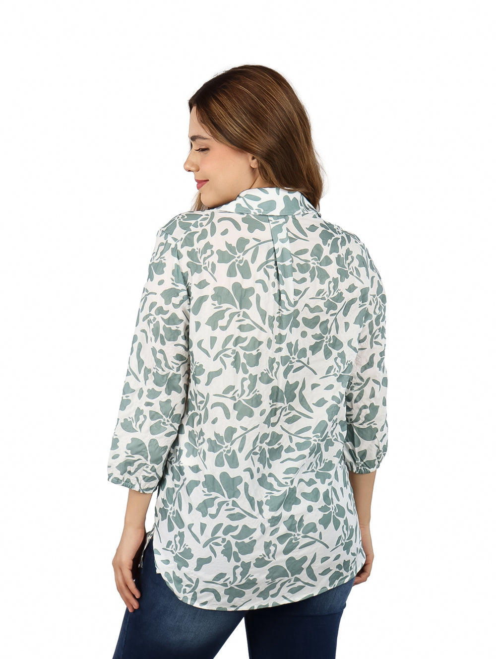 Mujer vistiendo una camisa blanca con estampado floral verde y pantalones azules.