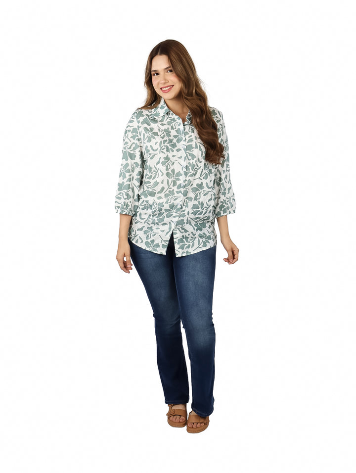 Mujer vistiendo una camisa blanca con estampado floral verde y pantalones azules.