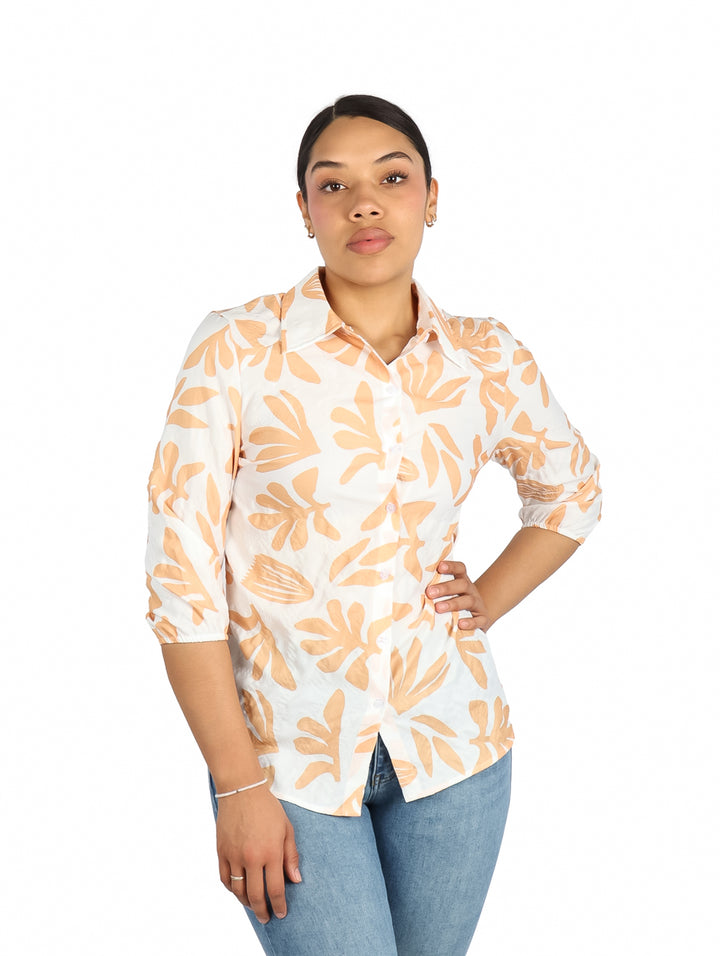 Mujer vistiendo camisa blanca de manga corta con estampado de hojas naranjas.