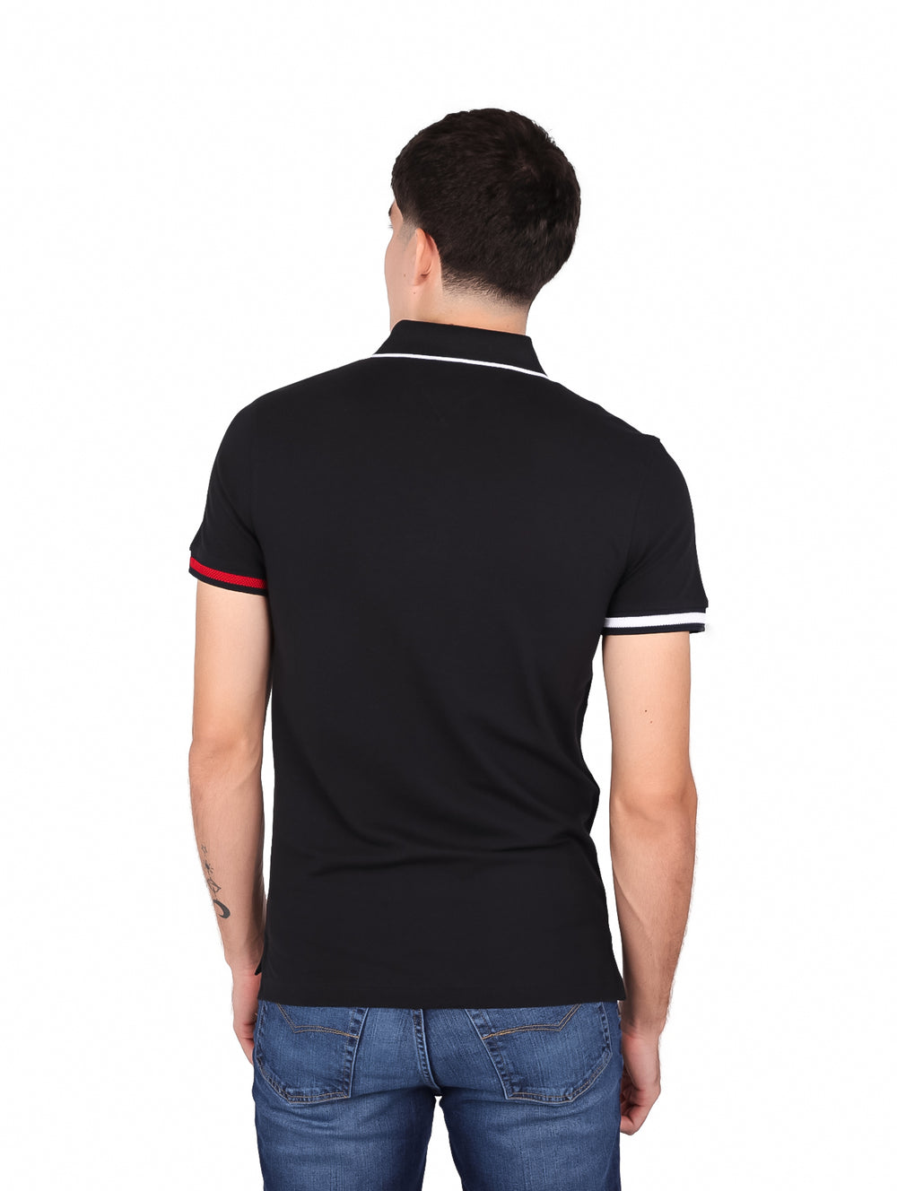 Hombre vistiendo polo negro Slim Fit de Tommy Hilfiger con detalles rojos y blancos en puños y cuello.