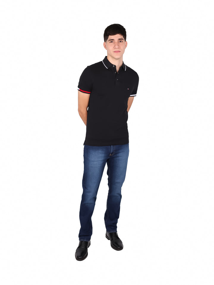 Hombre vistiendo polo negro Slim Fit de Tommy Hilfiger con detalles rojos y blancos en puños y cuello.