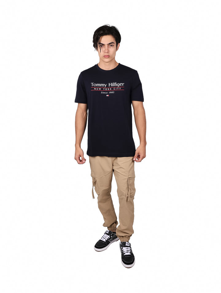 Hombre vistiendo camiseta azul marino de manga corta con texto de Tommy Hilfiger en el pecho.