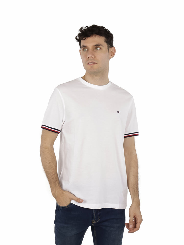 Hombre vistiendo una camiseta blanca de manga corta con rayas en los puños y un pequeño logo en el pecho.