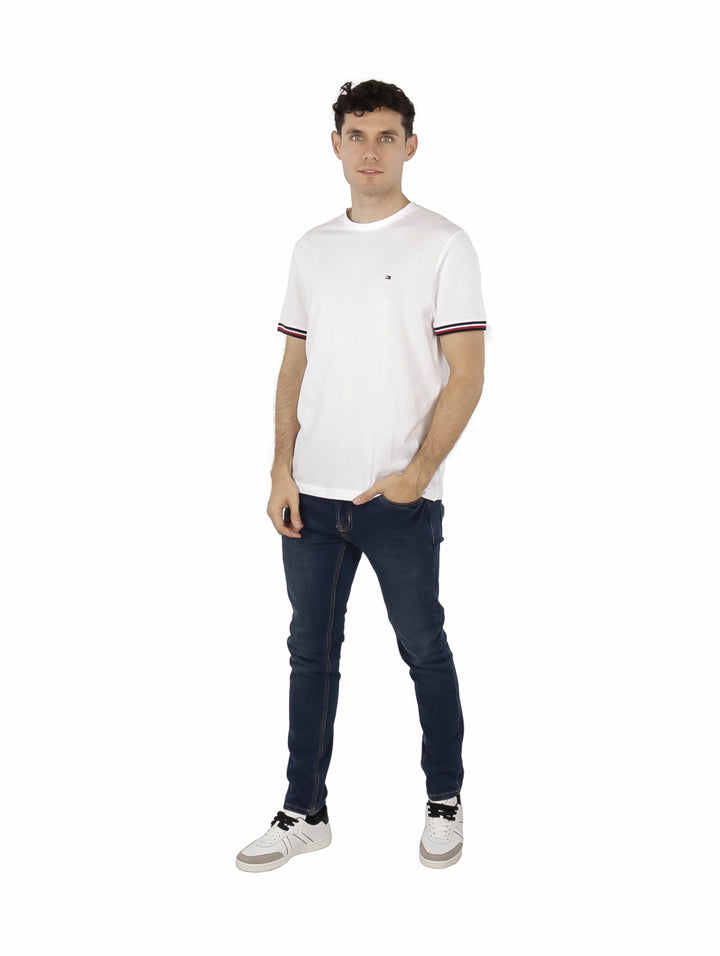 Hombre vistiendo una camiseta blanca de manga corta con rayas en los puños y un pequeño logo en el pecho.