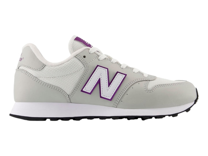 Tenis New Balance color blanco hueso con detalles en púrpura y suela blanca y negra.