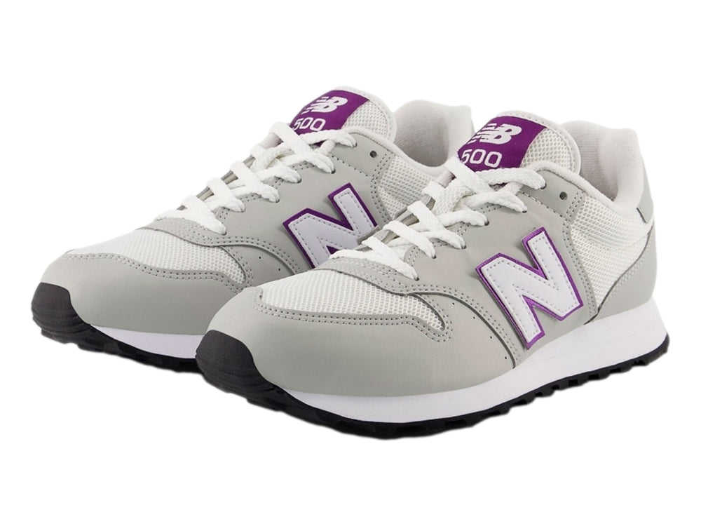 Tenis New Balance color blanco hueso con detalles en púrpura y suela blanca y negra.