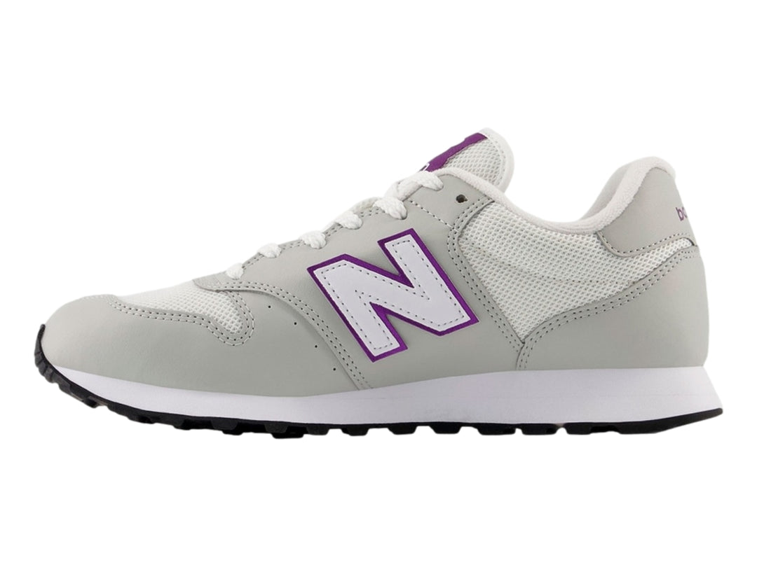 Tenis New Balance color blanco hueso con detalles en púrpura y suela blanca y negra.