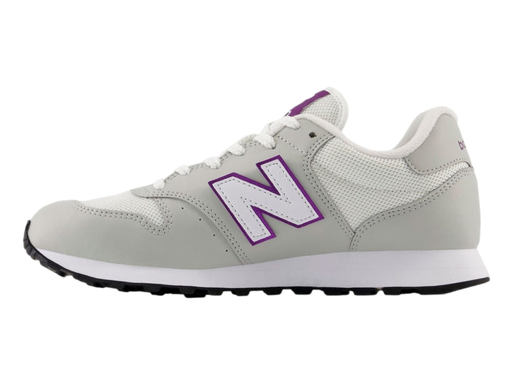 Tenis New Balance color blanco hueso con detalles en púrpura y suela blanca y negra.
