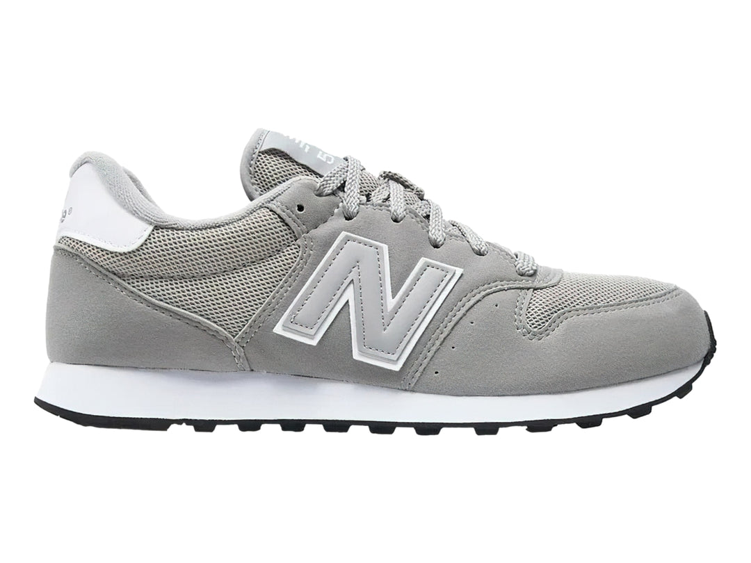 Tenis New Balance color gris con suela blanca y detalles en malla y gamuza.
