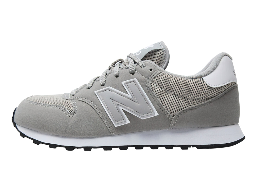 Tenis New Balance color gris con suela blanca y detalles en malla y gamuza.