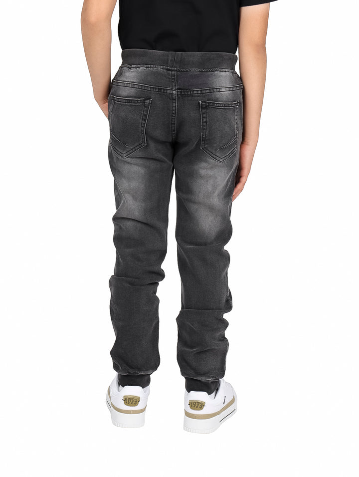 Pantalones jogger de mezclilla color negro con cintura elástica y cordón blanco para niño.