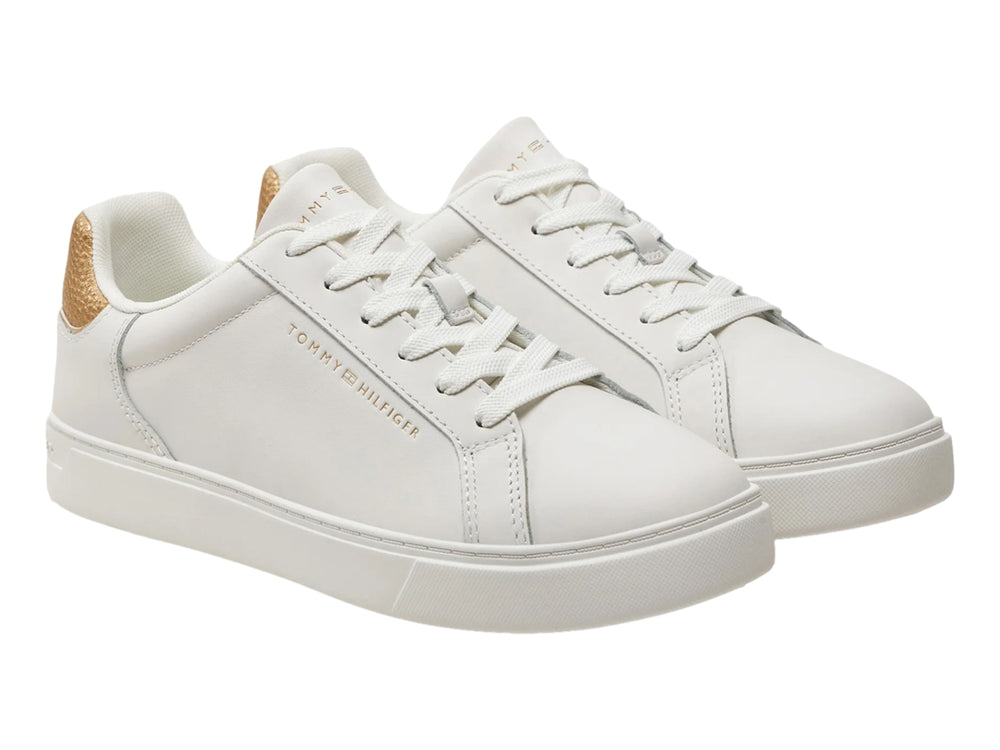 Tenis Tommy Hilfiger color ecru con detalle dorado metálico en el talón.