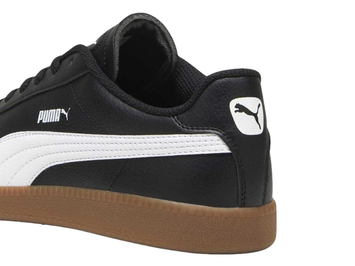 Tenis PUMA negros con franja blanca lateral y suela de goma color marrón.