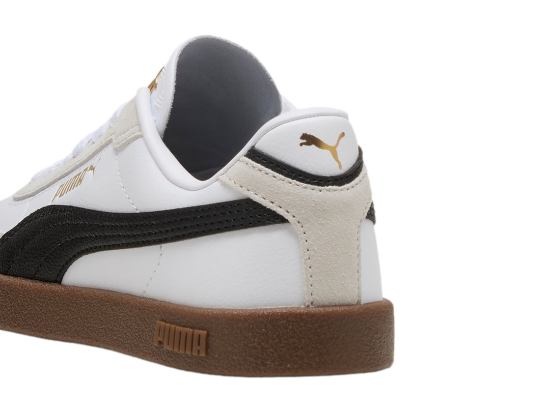 Tenis PUMA blancos para niños con franja negra lateral y suela de goma marrón.