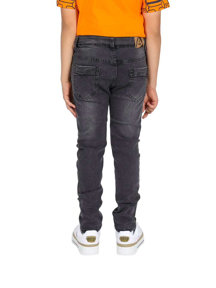 Pantalones vaqueros rectos de color negro para niño, combinados con camiseta naranja y tenis blancos.