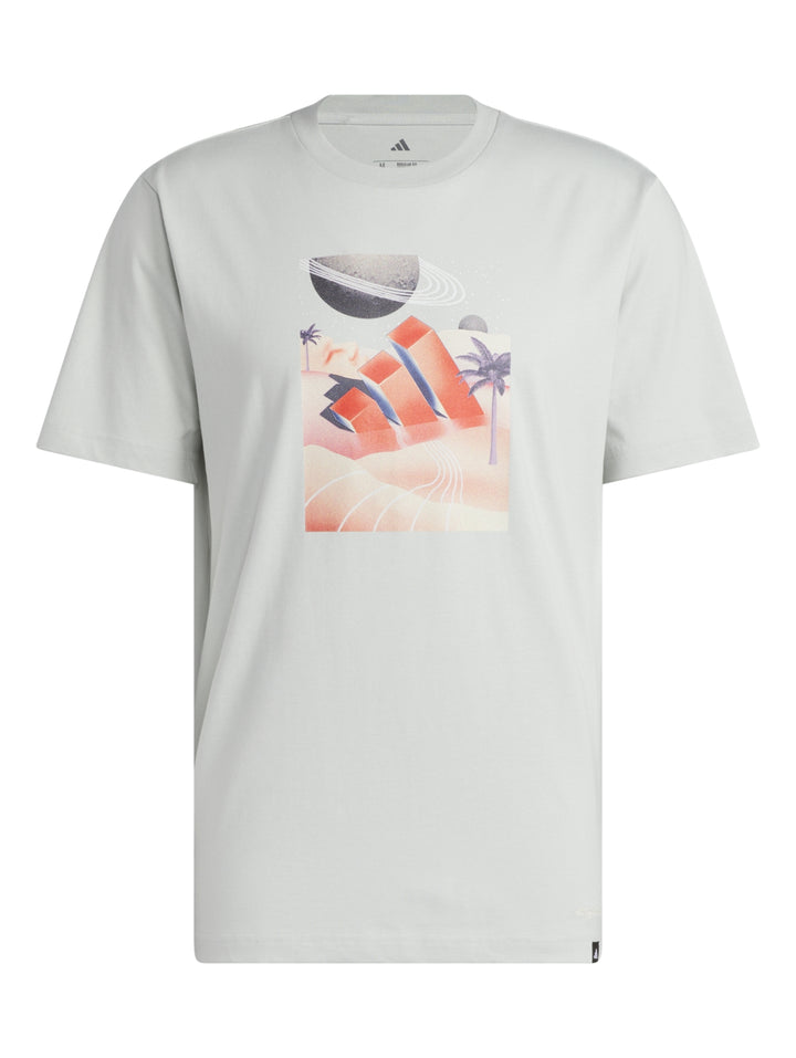 Hombre vistiendo camiseta blanca Adidas con estampado gráfico de paisaje playero en tonos naranja y azul.