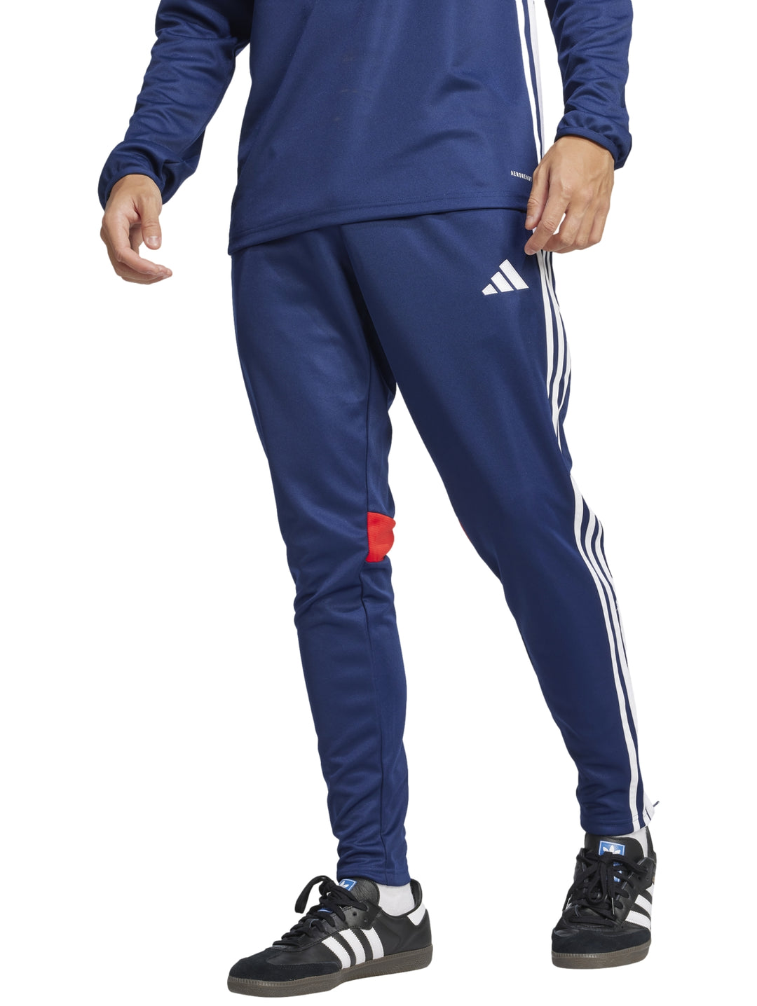 Pantalón deportivo Adidas azul marino con franjas blancas laterales y un pequeño detalle rojo en la pierna.
