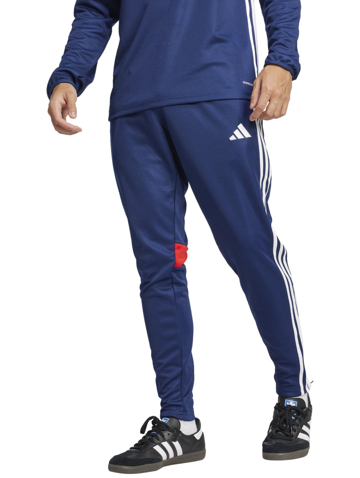 Pantalón deportivo Adidas azul marino con franjas blancas laterales y un pequeño detalle rojo en la pierna.