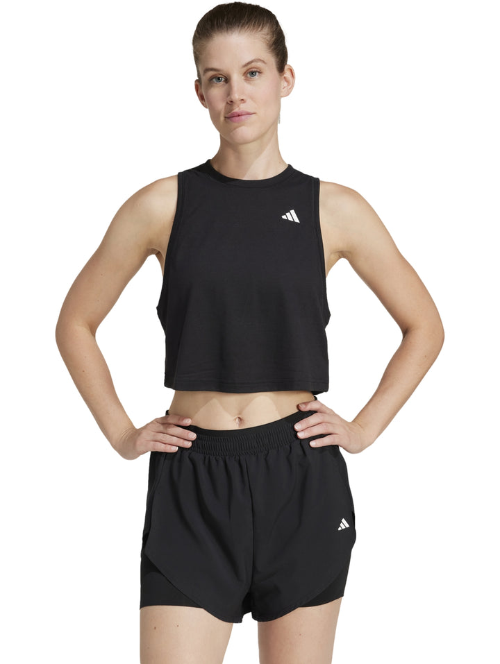 Mujer vistiendo un top deportivo negro sin mangas de corte boxy y shorts negros de la marca Adidas.