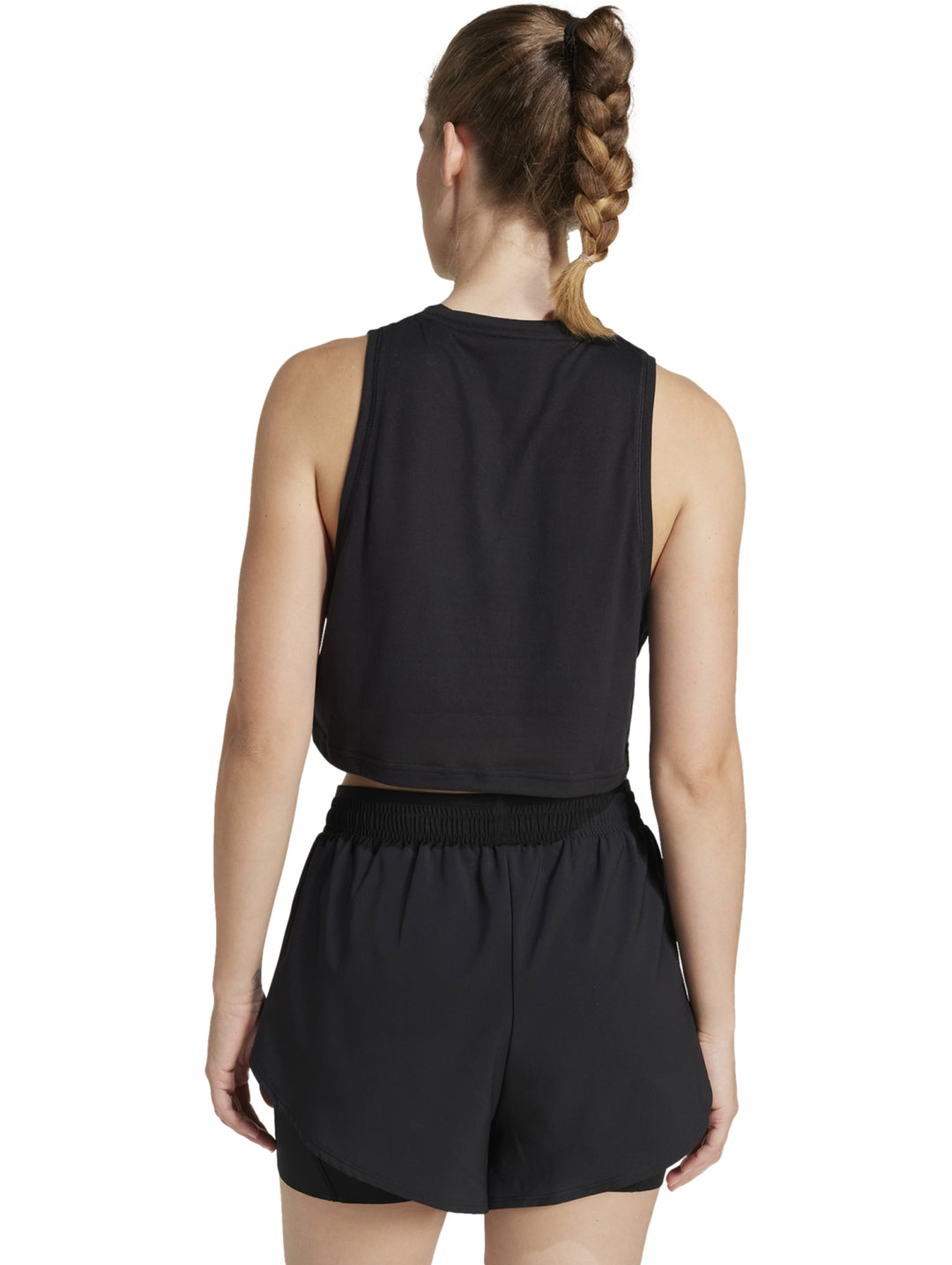 Mujer vistiendo un top deportivo negro sin mangas de corte boxy y shorts negros de la marca Adidas.