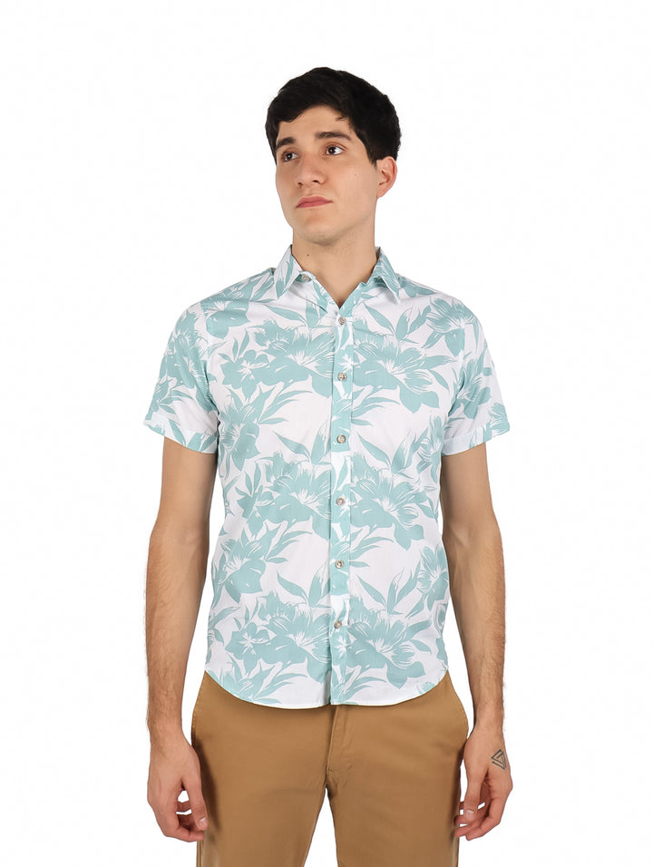 Hombre vistiendo camisa de manga corta blanca con estampado floral verde y pantalones color café.