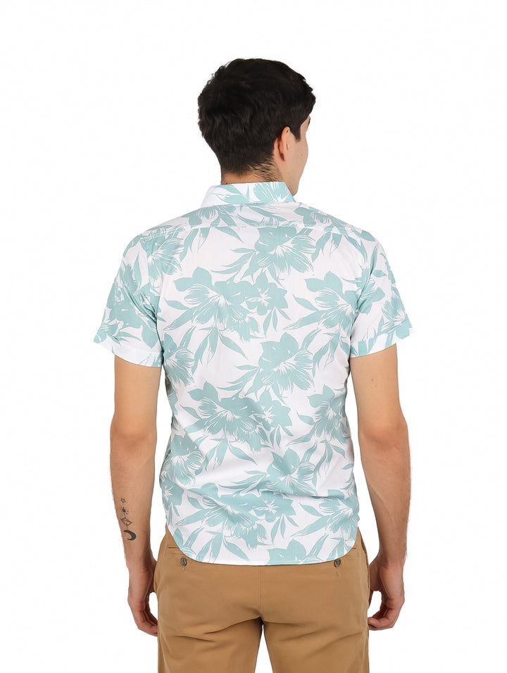 Hombre vistiendo camisa de manga corta blanca con estampado floral verde y pantalones color café.