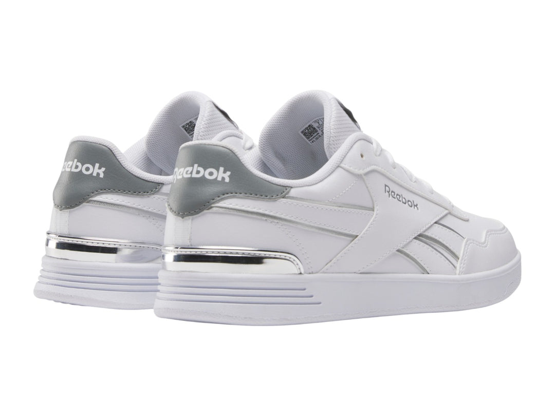 Tenis Reebok blancos de corte bajo con detalles plateados y suela blanca.