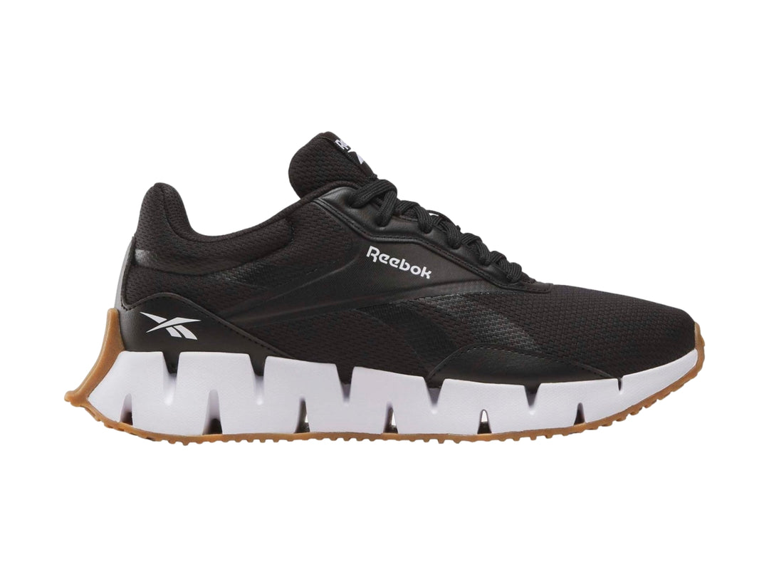 Tenis deportivos Reebok negros con suela blanca en zig-zag y base de goma marrón.