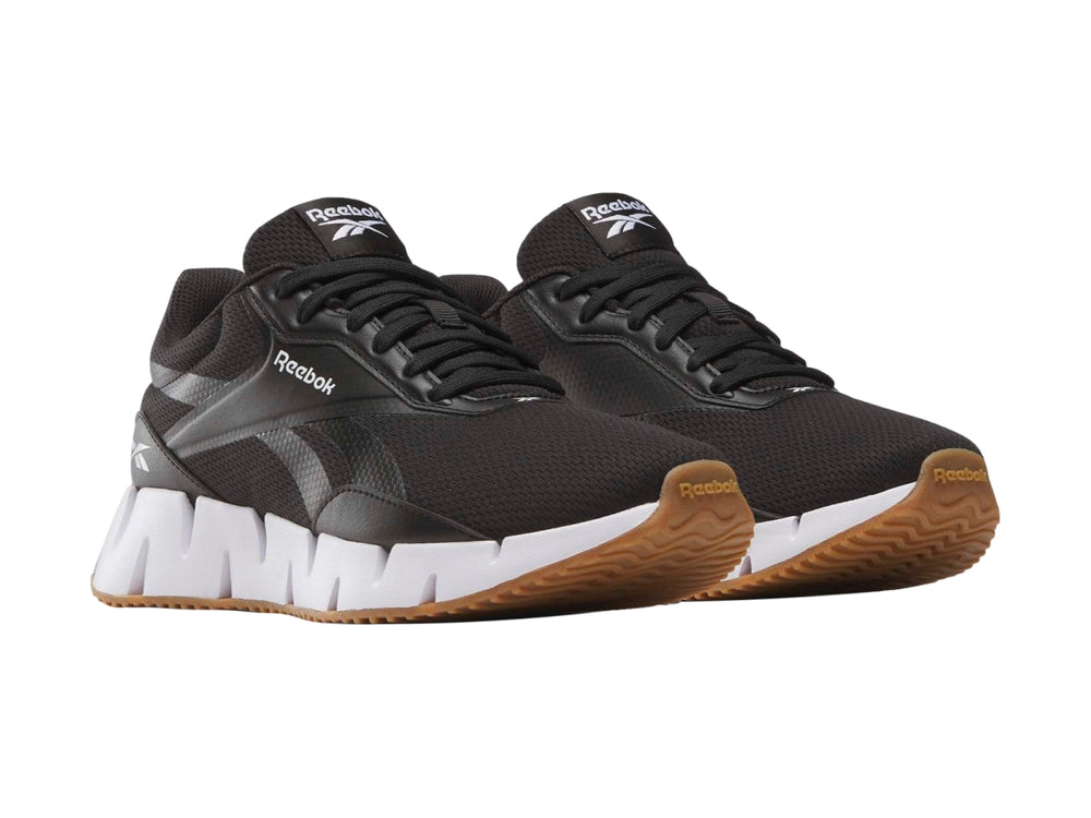 Tenis deportivos Reebok negros con suela blanca en zig-zag y base de goma marrón.