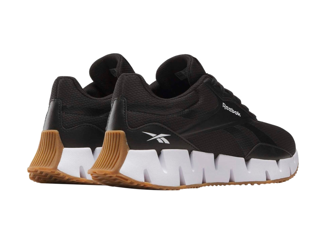 Tenis deportivos Reebok negros con suela blanca en zig-zag y base de goma marrón.