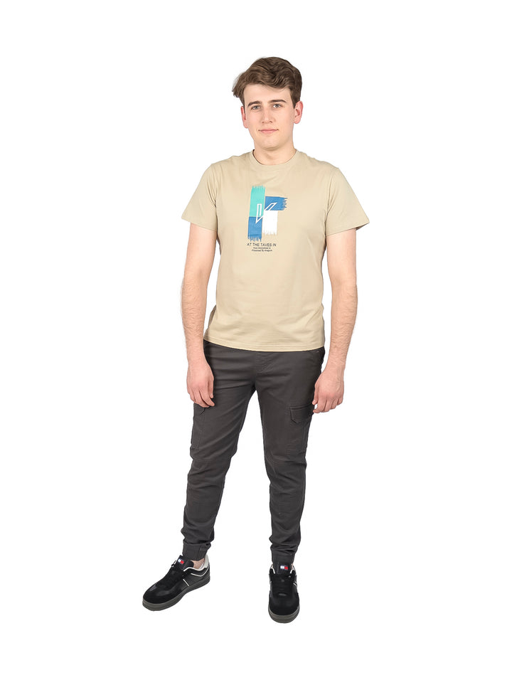 Hombre vistiendo playera color khaki de manga corta con estampado gráfico en el pecho y cuello redondo.
