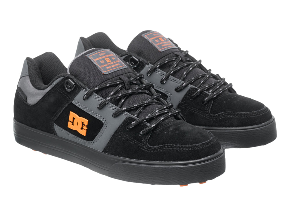Tenis DC Shoes color negro y gris con logotipo naranja y suela negra, vista lateral.