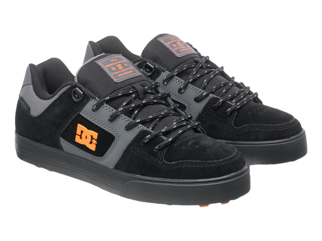 Tenis DC Shoes color negro y gris con logotipo naranja y suela negra, vista lateral.