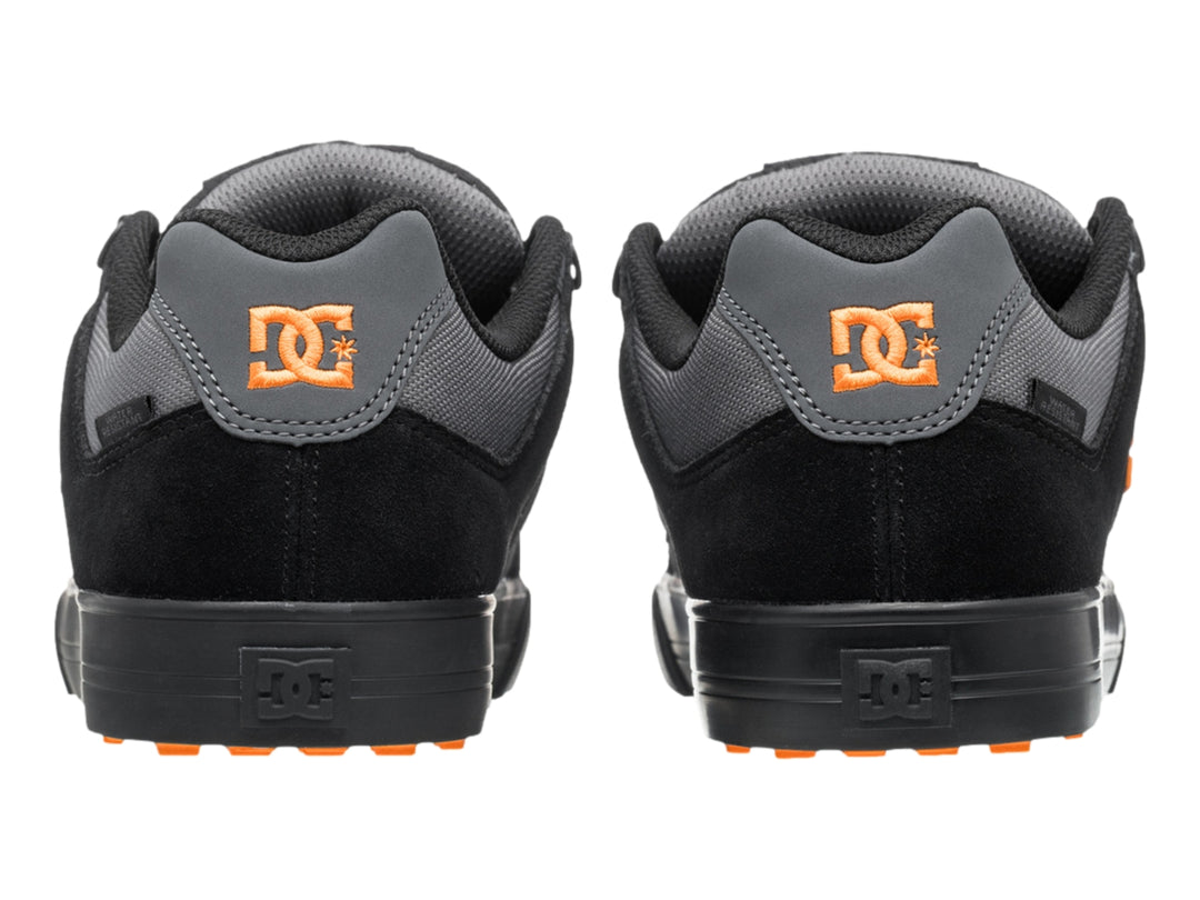 Tenis DC Shoes color negro y gris con logotipo naranja y suela negra, vista lateral.