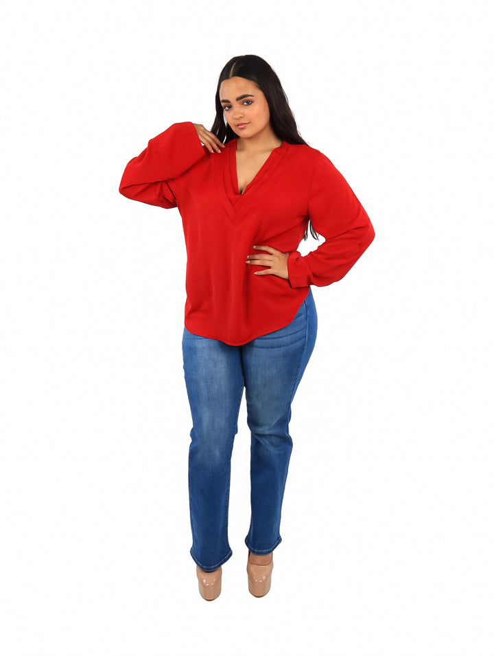 Mujer vistiendo una blusa roja de manga larga con cuello en V y pantalones azules.