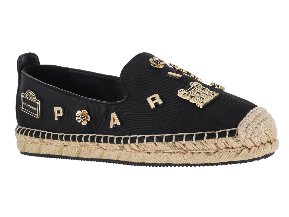Zapato plano tipo alpargata negro con suela de yute y pines metálicos dorados.