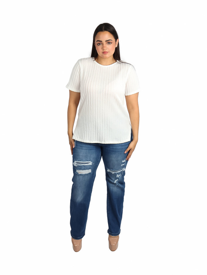 Mujer vistiendo una blusa blanca de manga corta con textura plisada y jeans azules.