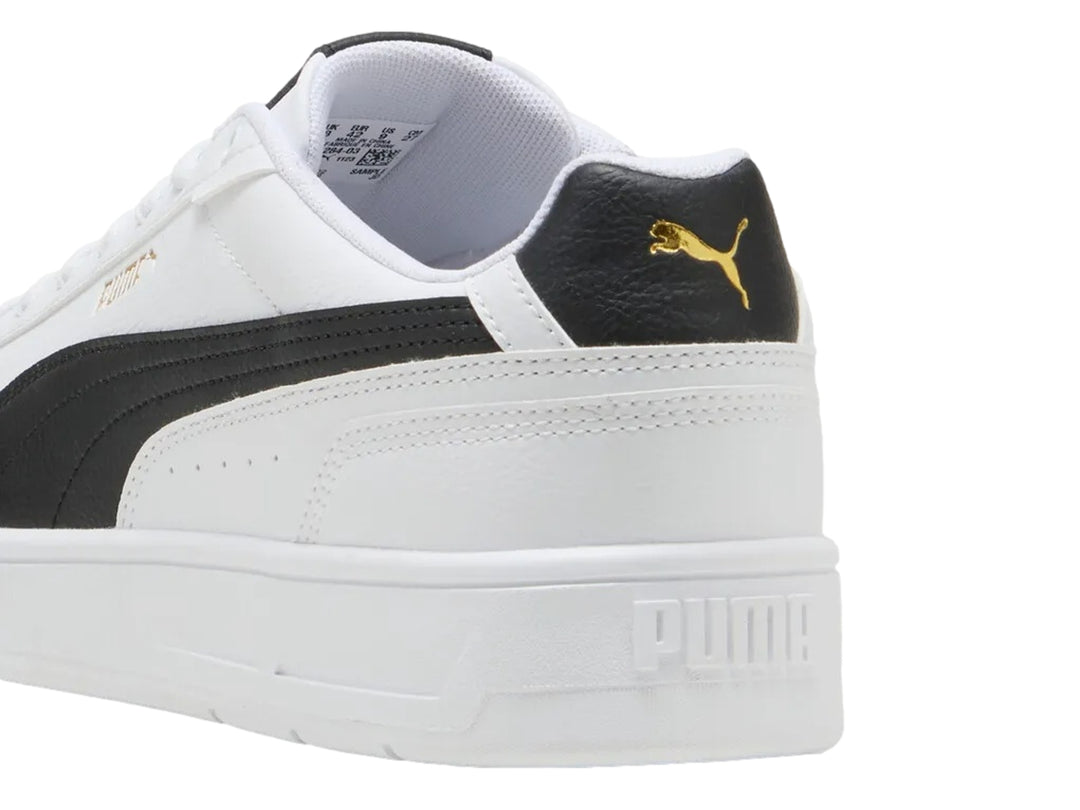 Tenis PUMA blancos con franja lateral negra y detalles dorados en la lengüeta.