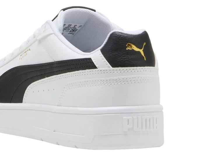Tenis PUMA blancos con franja lateral negra y detalles dorados en la lengüeta.