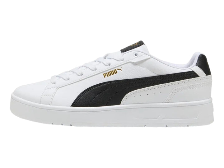 Tenis PUMA blancos con franja lateral negra y detalles dorados en la lengüeta.