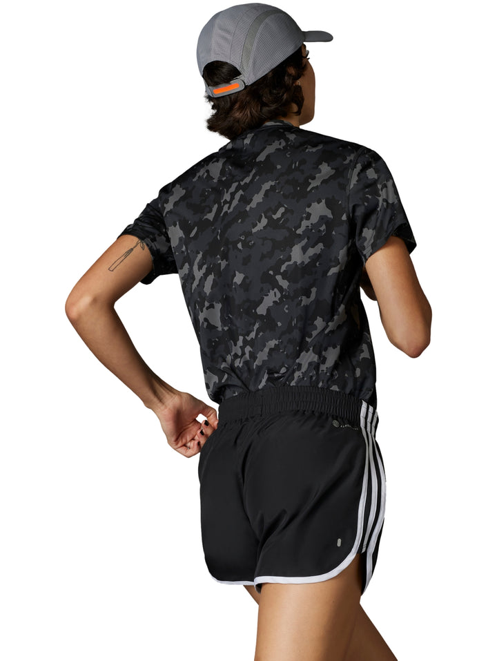 Mujer corriendo con shorts deportivos negros de marca Adidas con franjas blancas laterales.