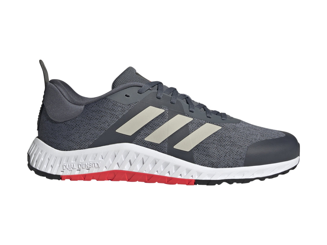 Tenis deportivos Adidas color gris con franjas blancas y suela blanca con detalle rojo en la base.