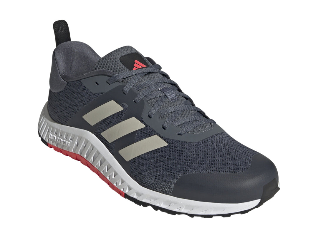 Tenis deportivos Adidas color gris con franjas blancas y suela blanca con detalle rojo en la base.