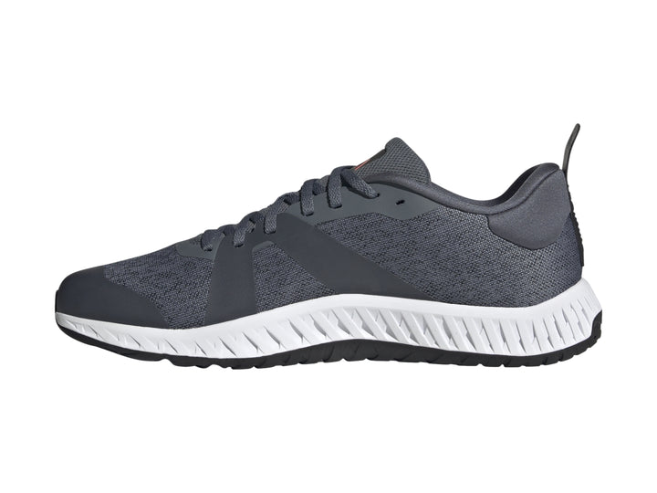 Tenis deportivos Adidas color gris con franjas blancas y suela blanca con detalle rojo en la base.